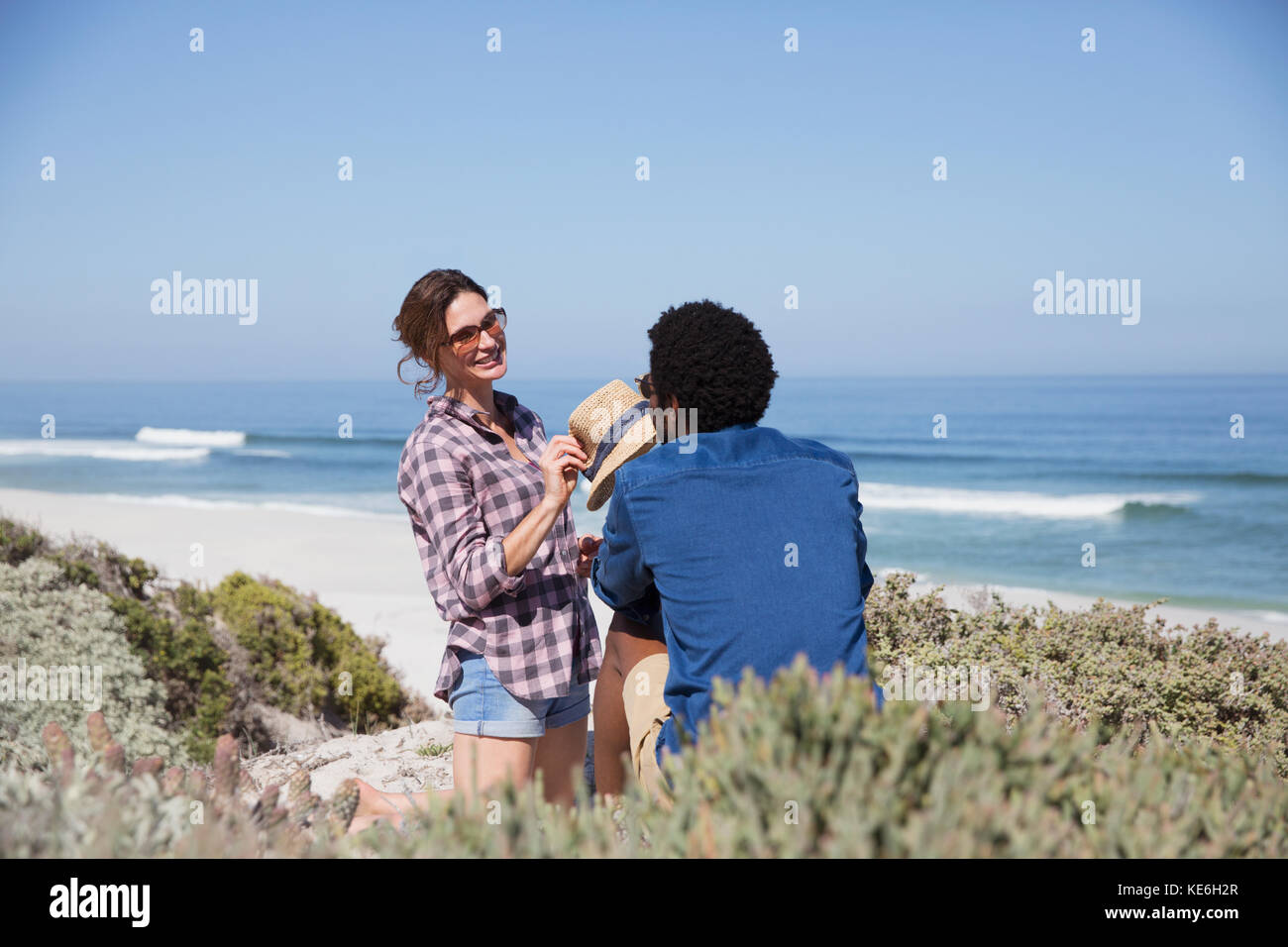 Sorridente coppia multietnica che parla sulla soleggiata spiaggia estiva Foto Stock