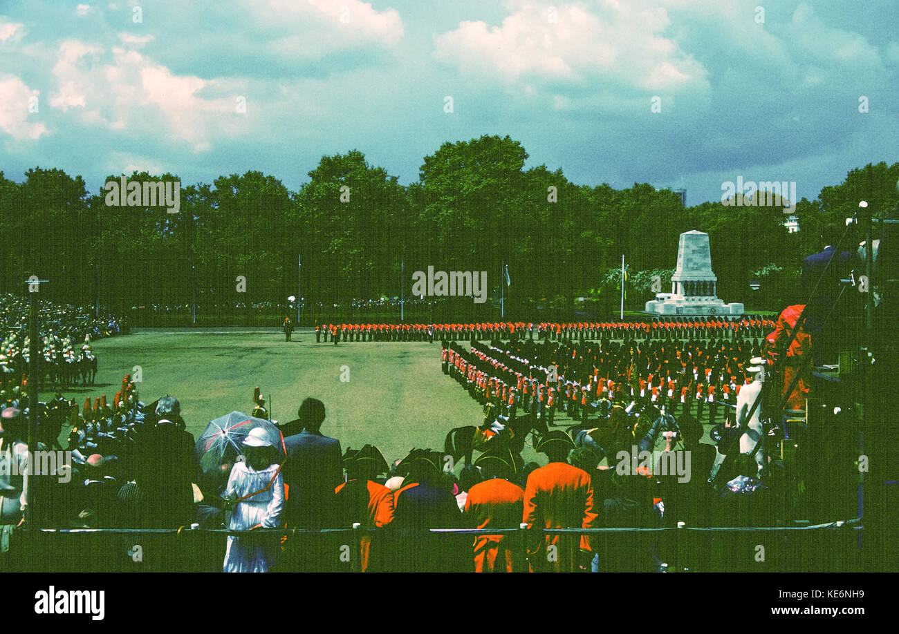 Trouping del colore in una giornata piovosa, con persone con ombrelli, vista da dover House, l'ufficio scozzese, Horse Guards Parade, Londra, Inghilterra, Regno Unito negli anni '80. Guards Memorial e folla tra cui Chelsea Pensioners e una donna in un abito bianco con un ombrello trasparente a baldacchino bolla Foto Stock