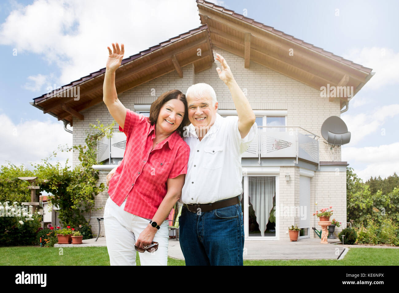 Felice coppia Senior alzando le braccia davanti a casa Foto Stock