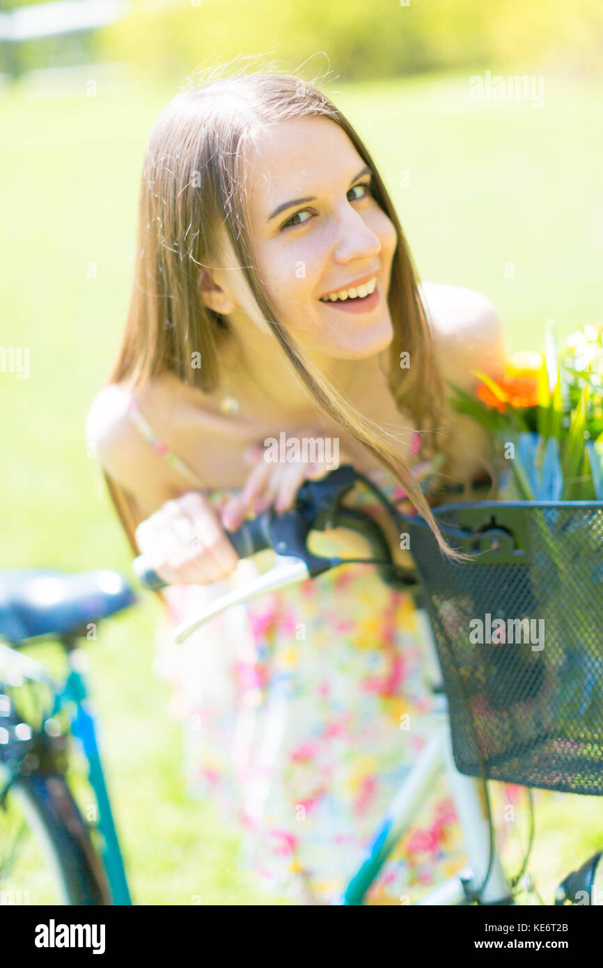 Ritratto di giovane bella donna con capelli lunghi in estate park. accanto a una bicicletta con un cestino di fiori Foto Stock
