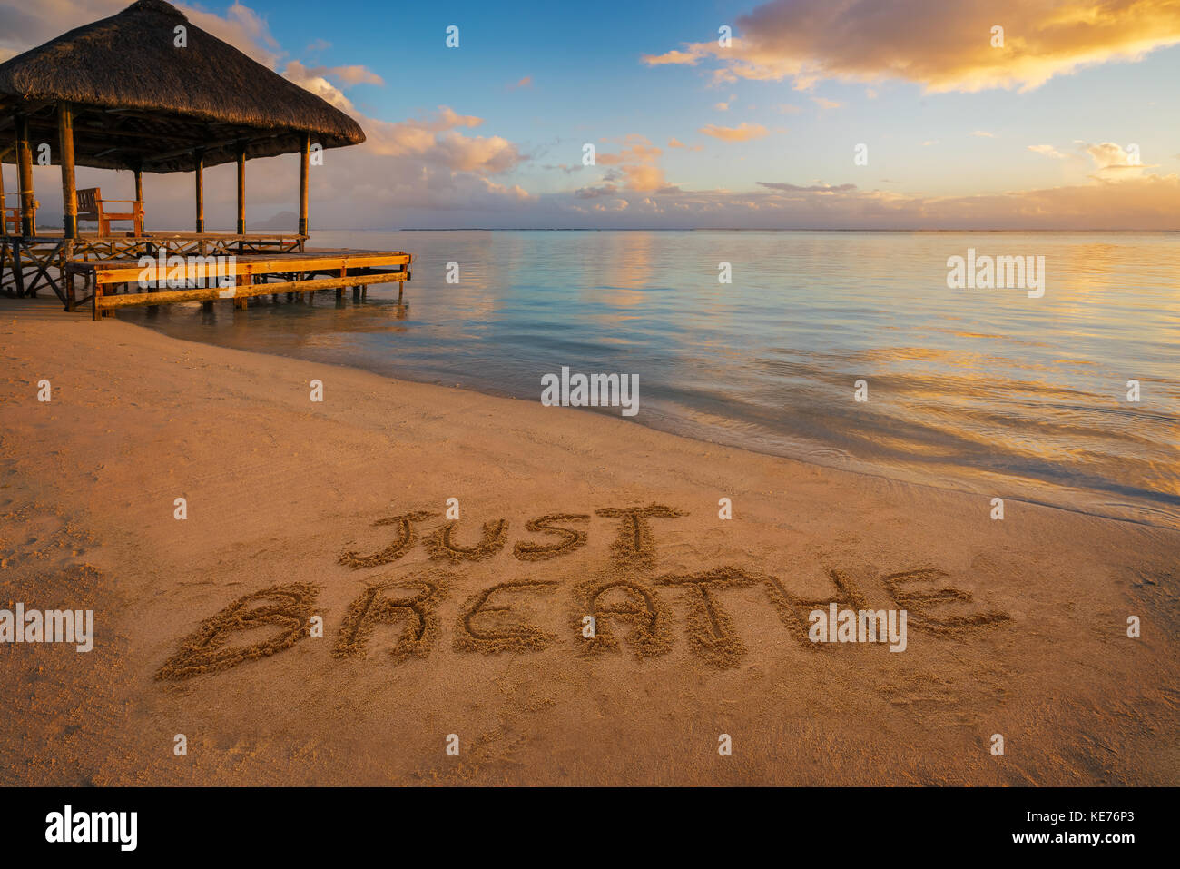 Primo piano scritto nella sabbia 'appena respirare' al tramonto in isola Maurizio con pontile sul lato sinistro. Foto Stock
