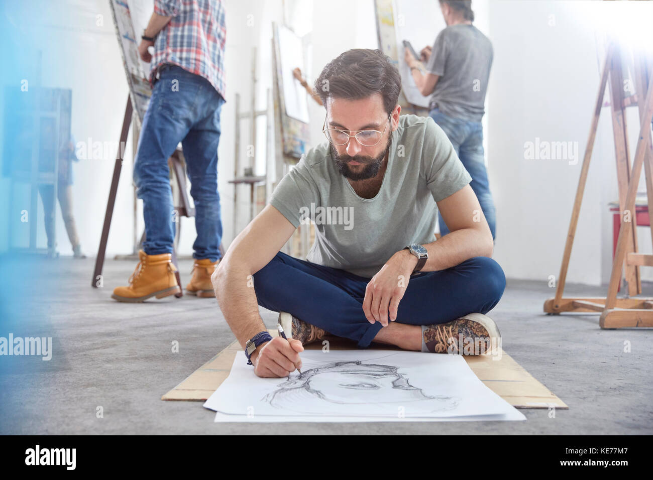 Artista maschile seduto a gambe incrociate schizzi sul pavimento in classe d'arte studio Foto Stock