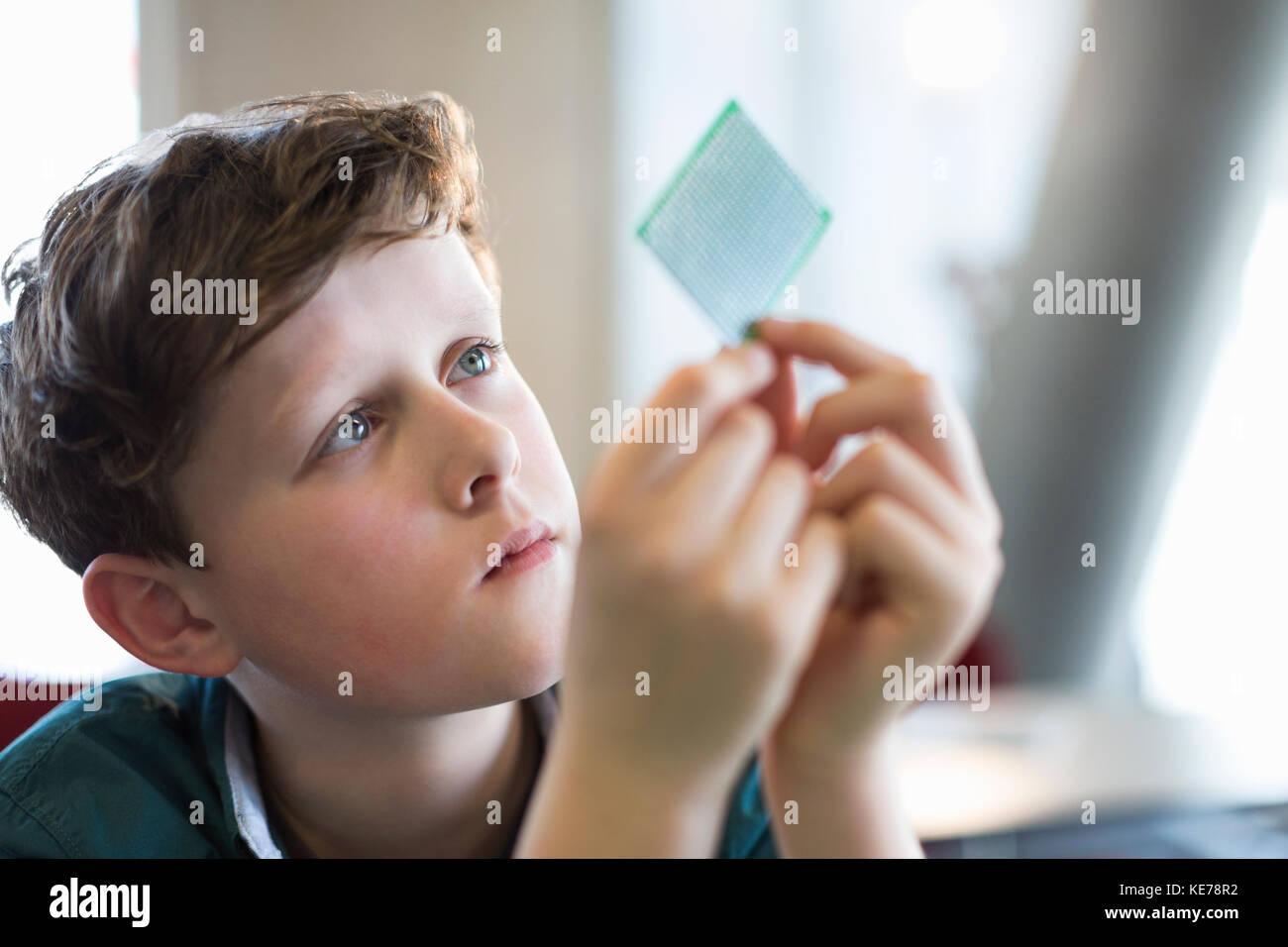 Ragazzo curioso e concentrato che esamina il chip del computer in classe Foto Stock