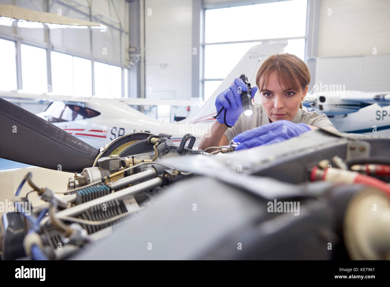 Femmina focalizzato ingegnere meccanico con torcia elettrica esaminando motore aereo in hangar Foto Stock