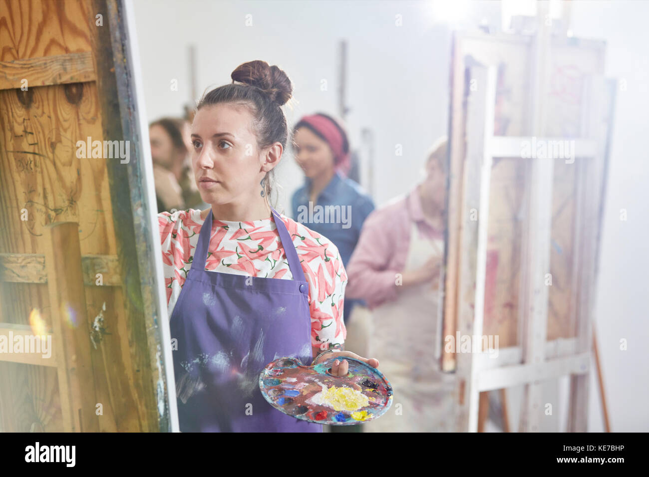 Artista femminile focalizzato con pittura di tavolozza a easel in arte studio di classe Foto Stock