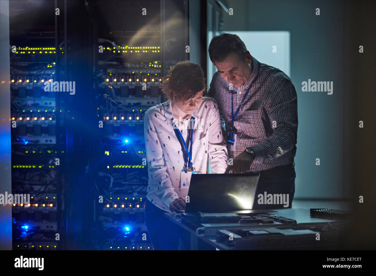 Tecnici IT che lavorano su un computer portatile in una sala server buia Foto Stock
