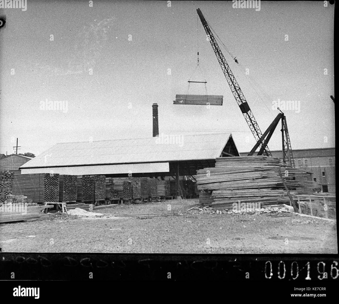 Questa fotografia mostra una gru in azione, impilando legname in un cantiere o in un sito industriale. Mette in evidenza l'uso di macchinari pesanti nella movimentazione e nell'organizzazione efficiente dei materiali da costruzione. Foto Stock