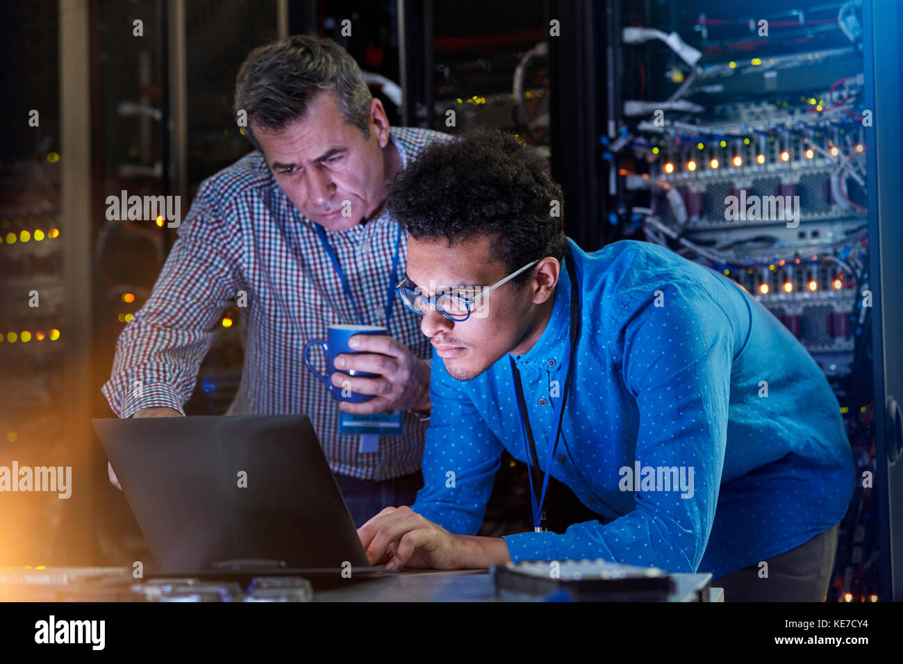 Tecnici IT maschili concentrati che lavorano su notebook in un server buio camera Foto Stock