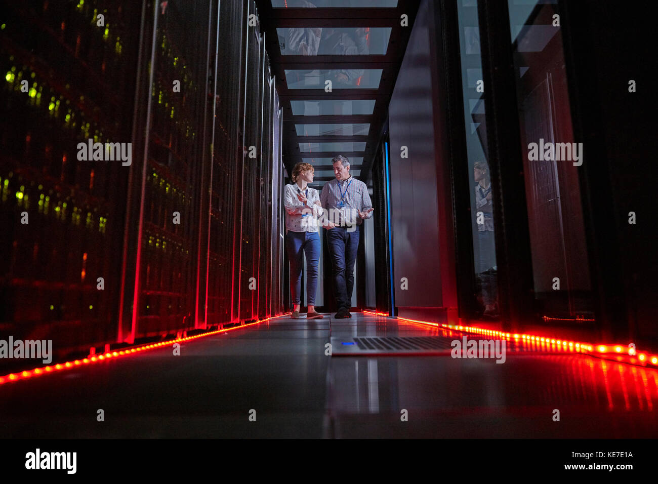 I tecnici IT parlano e camminano nella stanza dei server buia Foto Stock