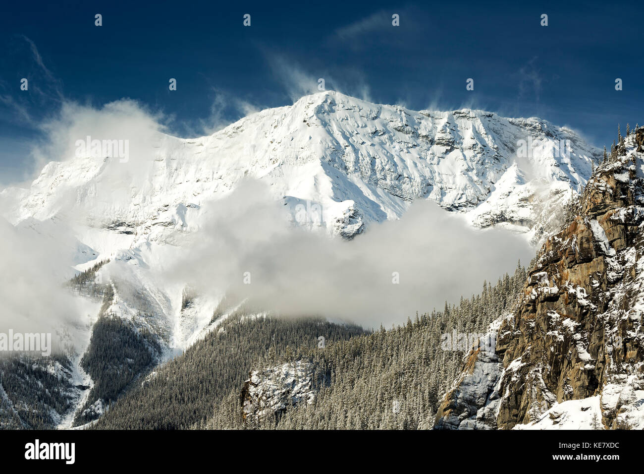 Coperta di neve montagna con nebbia e neve coperti di alberi con cielo blu; Alberta, Canada Foto Stock