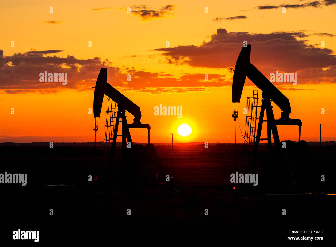 Silhouette di due Pumpjacks presso Sunrise con un colorato arancione il sole, le nuvole e il cielo; Alberta, Canada Foto Stock