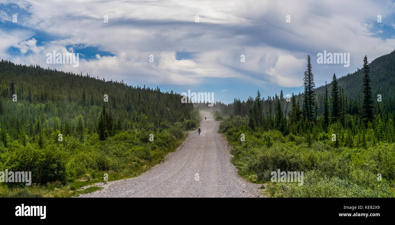 Due ciclisti corsa giù per una strada di ghiaia tra colline e foreste; Canada Foto Stock