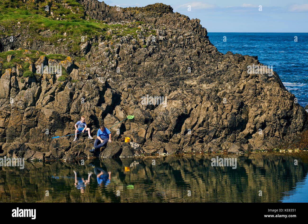 Un padre e figlio la pesca nelle pozze di marea lungo la costa dell'Irlanda del Nord; Irlanda Foto Stock