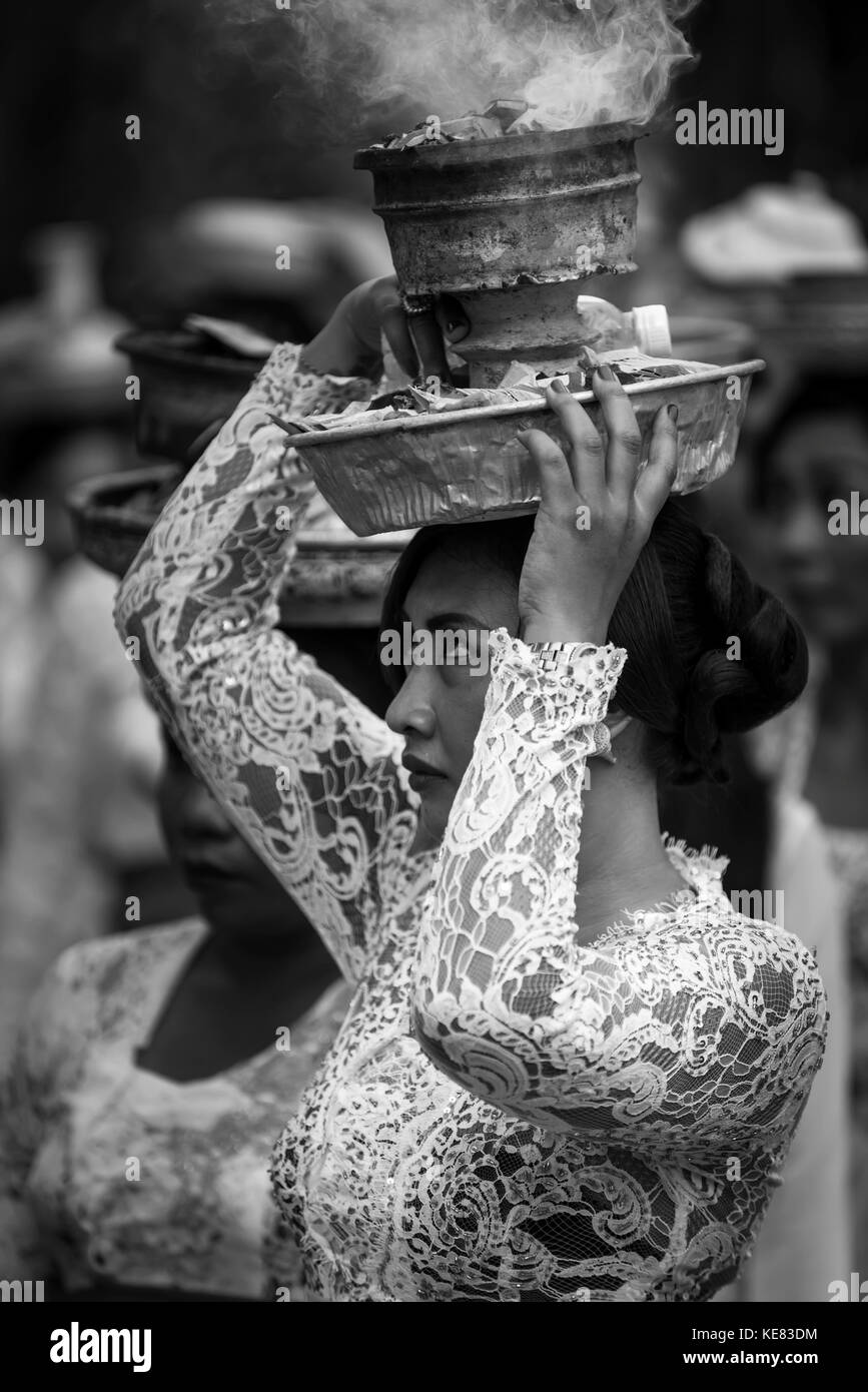 Una giovane donna ad una cerimonia religiosa che porta una fumatori offre sul suo capo; Bali, Indonesia Foto Stock