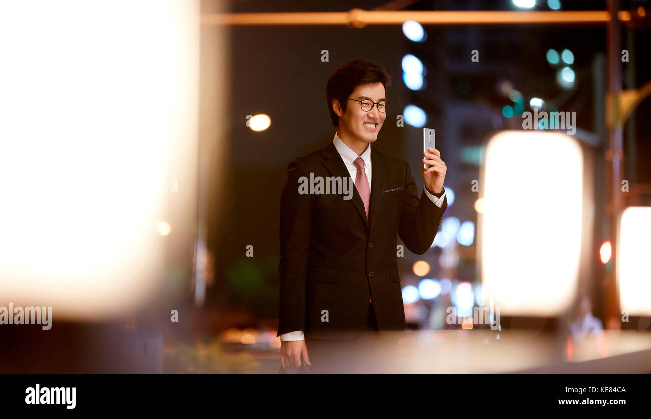 Imprenditore sorridente holding smartphone nella città di notte Foto Stock