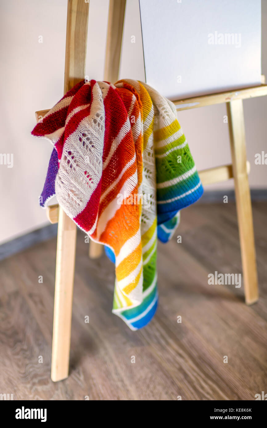 Un frammento di un fatti a mano multi-colore sciarpa lavorata a maglia in un interno di casa su un cavalletto. I colori del arcobaleno. Il concetto di comfort abitativo, ricamo, kni Foto Stock