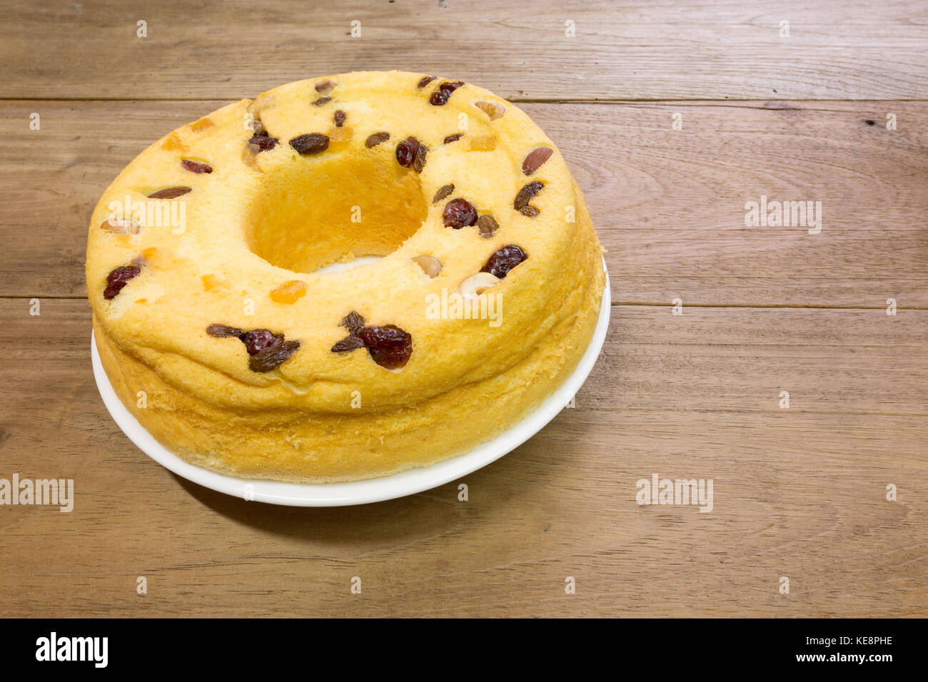 Torta di cotone, miscela di frutti di mandorla, noci di anacardi, mirtilli rossi, mango secchi, uvetta verde, su piatto bianco, pronto a mangiare, su un rustico tavolo di legno Foto Stock