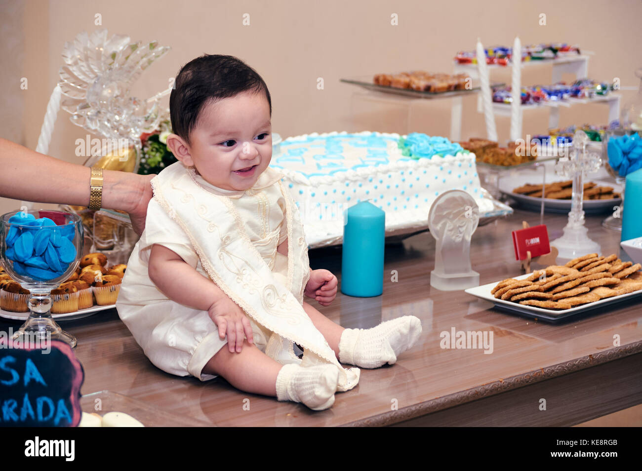 Battezzato bambino seduto sul tavolo da festa dolci Foto Stock