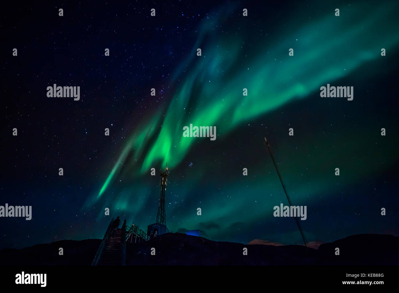 Onde verdi di aurora boreale con stelle lucenti oltre le montagne e la torre della radio, Nuuk, Groenlandia Foto Stock
