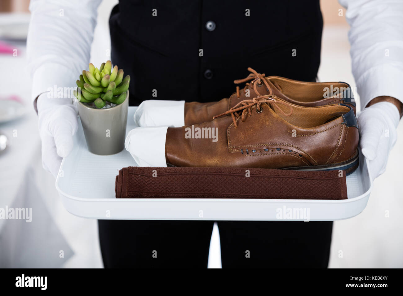 Close-up di butler che trasportano paio di scarpe marrone e piccoli cactus vaso sul vassoio di plastica Foto Stock