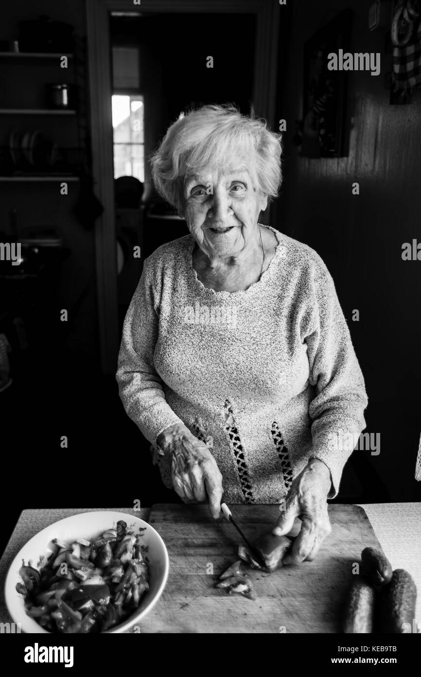 Una donna anziana in cucina trita verdure per insalata. foto in bianco e nero. Foto Stock