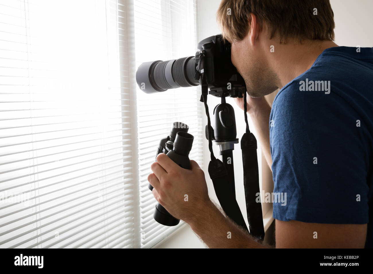 Giovane fotocamera da presa maschio fotografando attraverso le persiane a casa Foto Stock