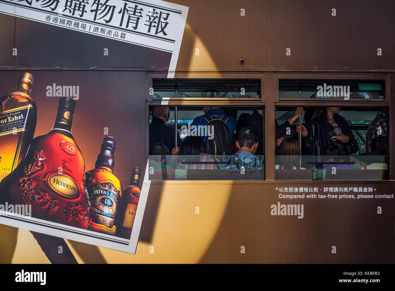 Passeggeri che viaggiano su un tram di Hong Kong che pubblicizza spiriti Foto Stock