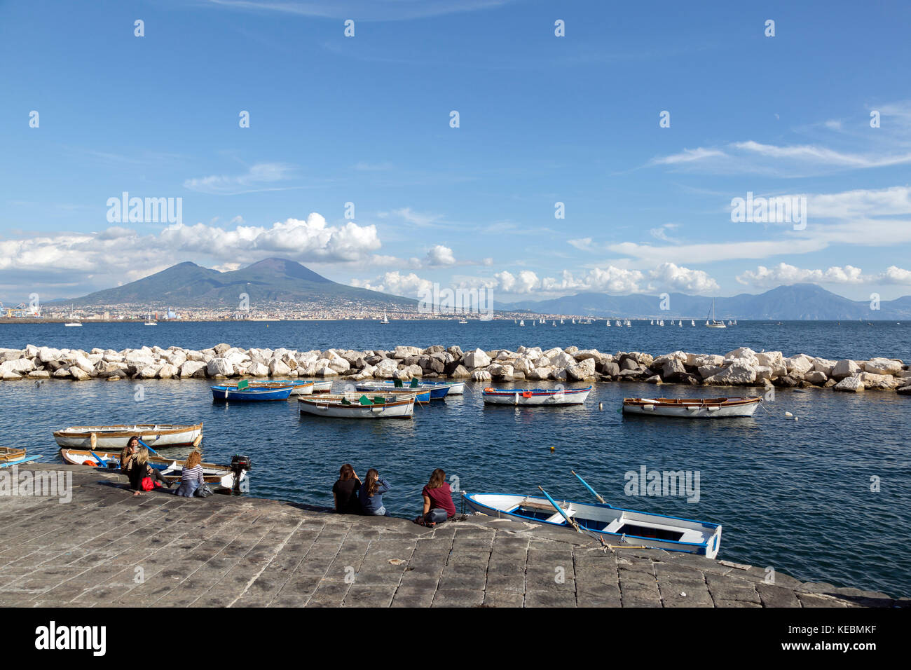Scena costiere del golfo di Napoli, wth turisti, barche da pesca costa rocciosa. Barche a vela e il Vesuvio sullo sfondo Foto Stock