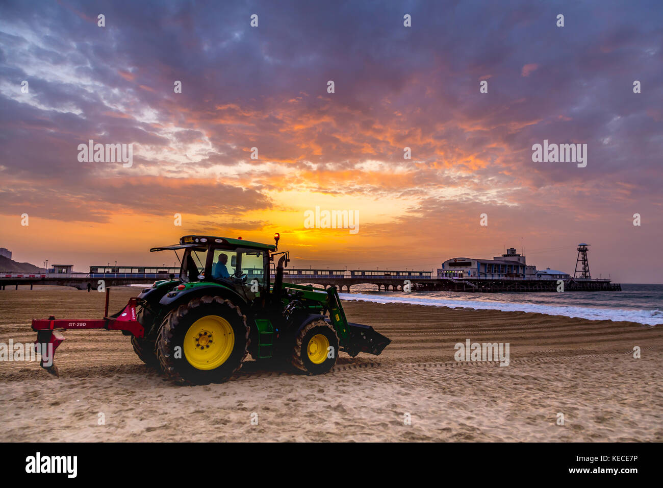 Un trattore appiattisce la sabbia sulla spiaggia vicino al molo di Bournemouth, un molo vittoriano con un divertimento arcade, un teatro di varietà e il cafe Foto Stock