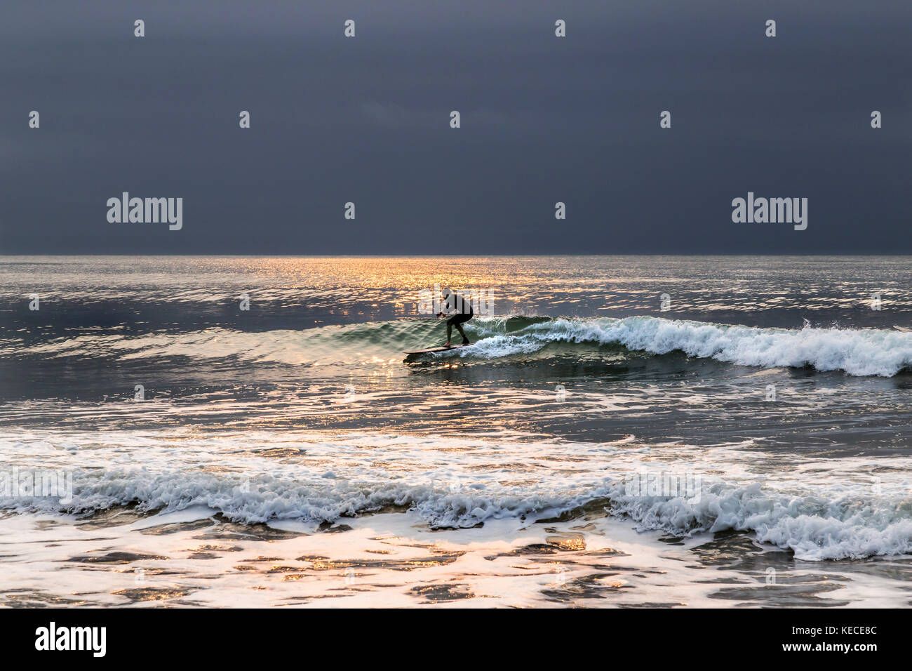 Surf vicino al molo di Bournemouth con il RISING SUN colata di un bagliore giallo sull'acqua Foto Stock