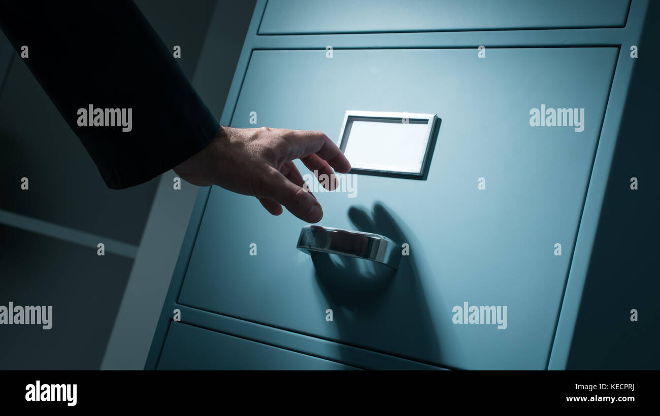 Lavoratore di ufficio ricerca top secret informazioni riservate in ufficio fino a tarda notte, il furto di dati e il concetto di sicurezza Foto Stock