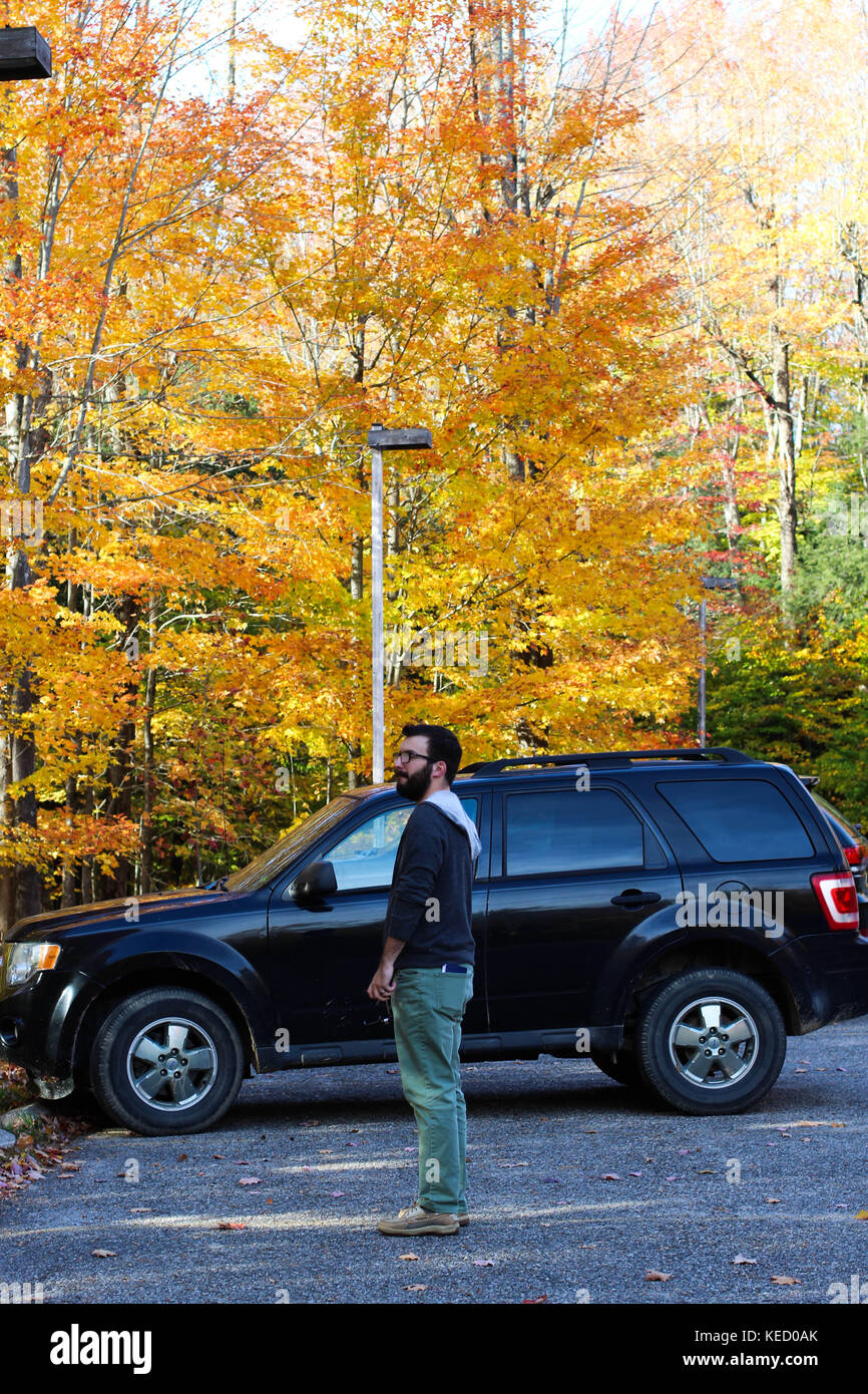 Un uomo in piedi in un parcheggio di un parco statale nel nord del Michigan circondato da colori autunnali e partenze a ottobre Foto Stock