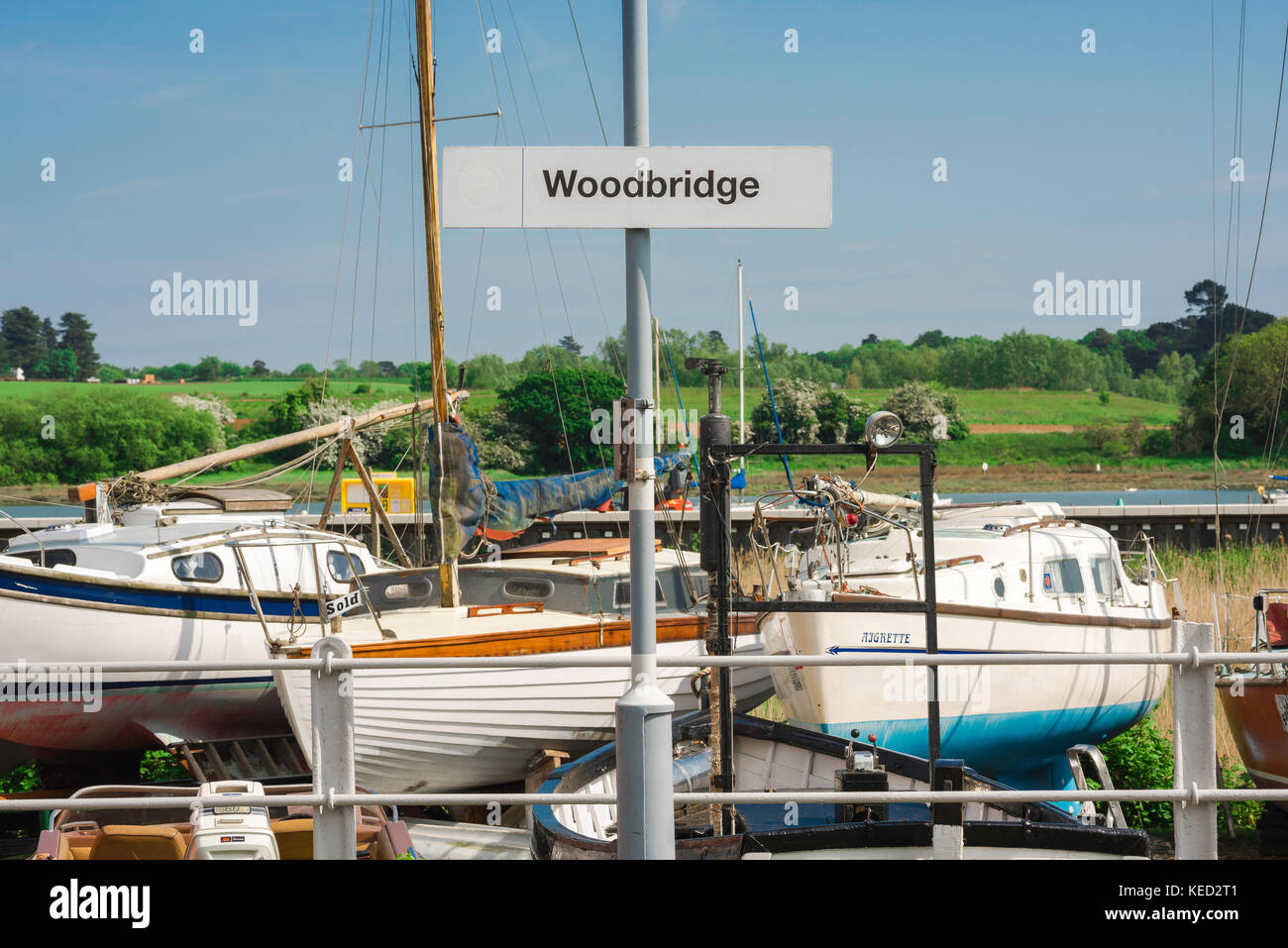 Città di Woodbridge Suffolk, vista della stazione ferroviaria della città, segno di piattaforma di fronte alle barche a vela accanto al fiume Deben a Woodbridge, Suffolk, Regno Unito. Foto Stock
