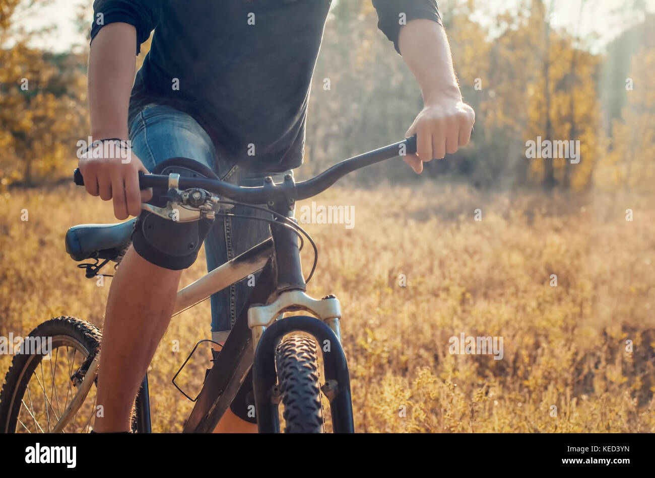 Atletica Giovane uomo in una t-shirt nera e blu jeans corti sulla bicicletta sportiva su un luminoso autunno sfondo. l'immagine mostra un frammento di un modulo di interconnessione BIC Foto Stock