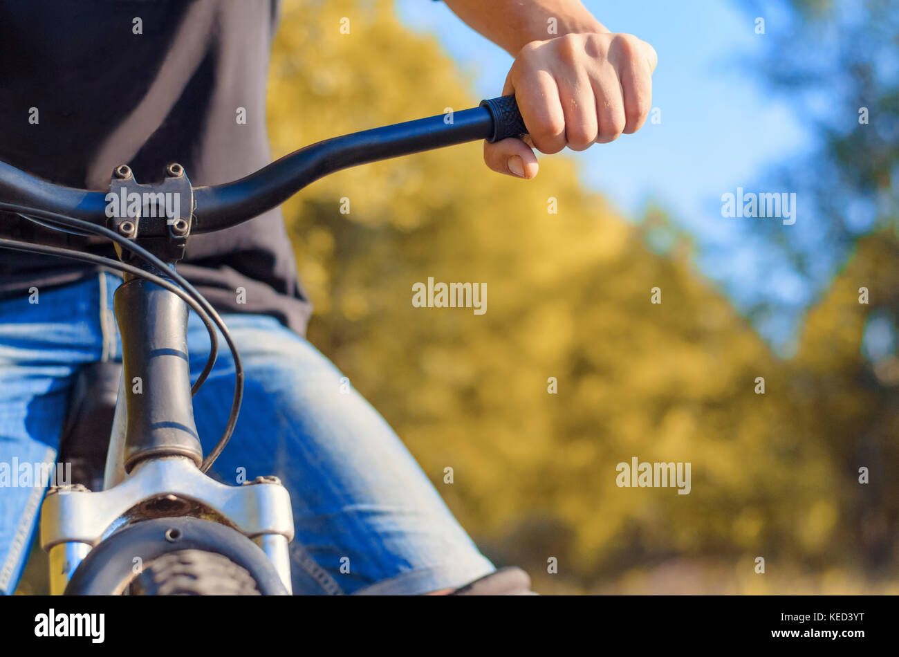 Close-up di una mano di un uomo in jeans e una t-shirt nera al volante di una bicicletta fuoristrada. a piedi in aria aperta in autunno. Foto Stock