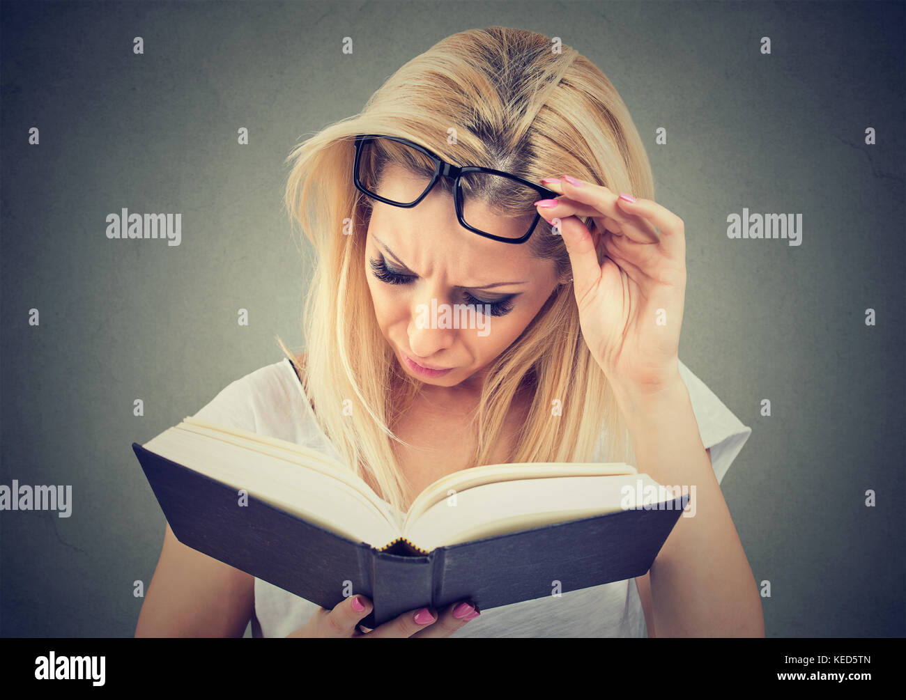 Donna con gli occhiali che soffrono di affaticamento della vista dopo la lettura di un libro Foto Stock