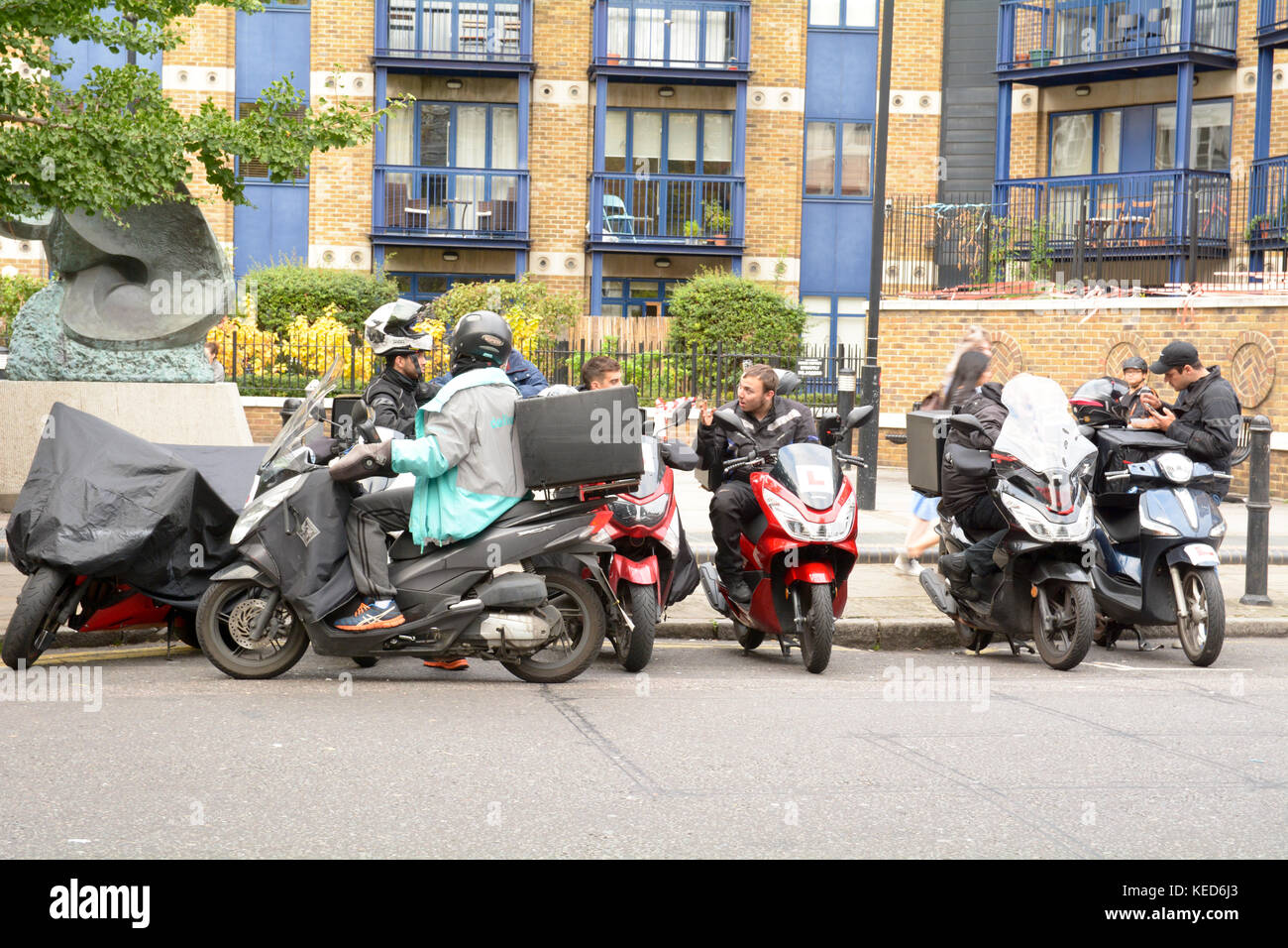 Gruppo di piloti di consegna tra cui un pilota Deliveroo avente una pausa al di fuori di Spitalfields Market in London Inghilterra England Foto Stock