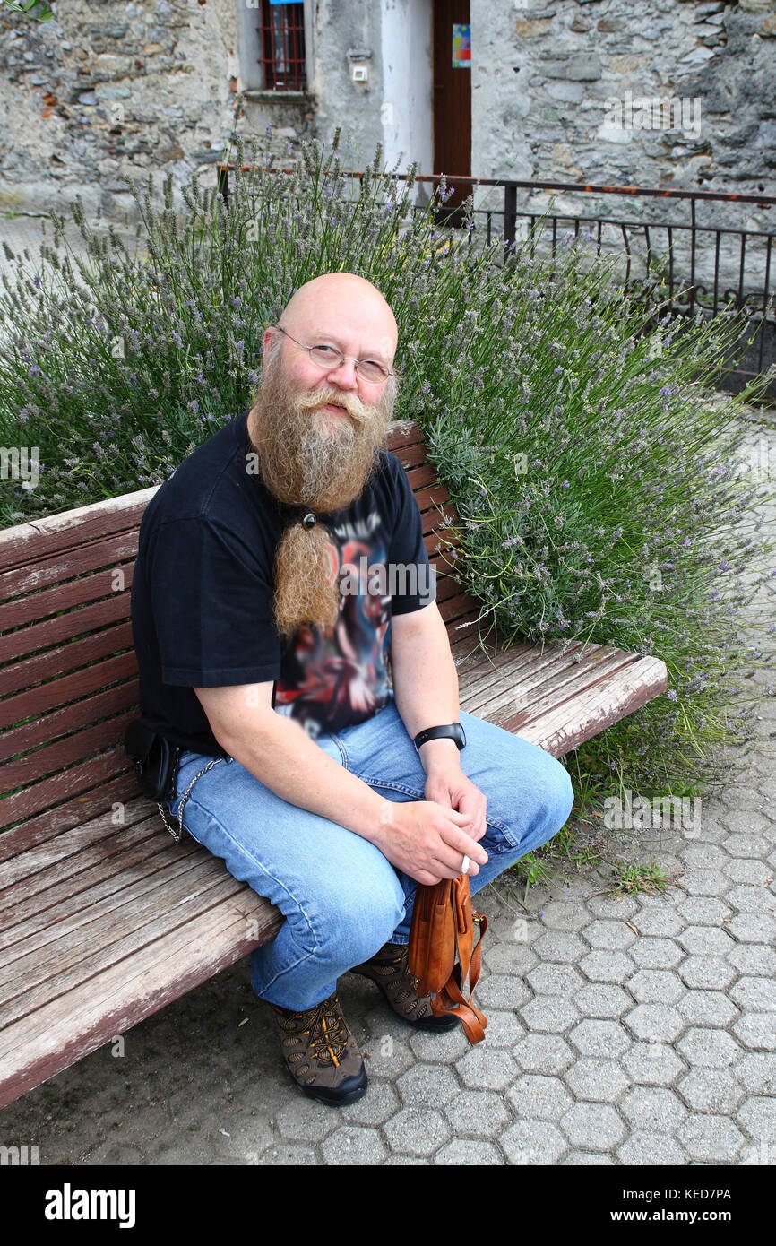 Ein Mann mit langem Bart sitzt auf einer Sitzbank Foto Stock