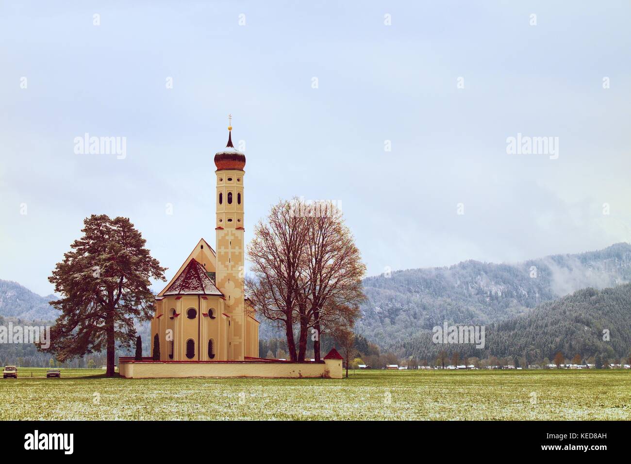 Vecchia chiesa con alto campanile e cimitero bellow montagne. aprile meteo. primavera umida di neve in già fresco verde erba di prato mountai a soffietto Foto Stock