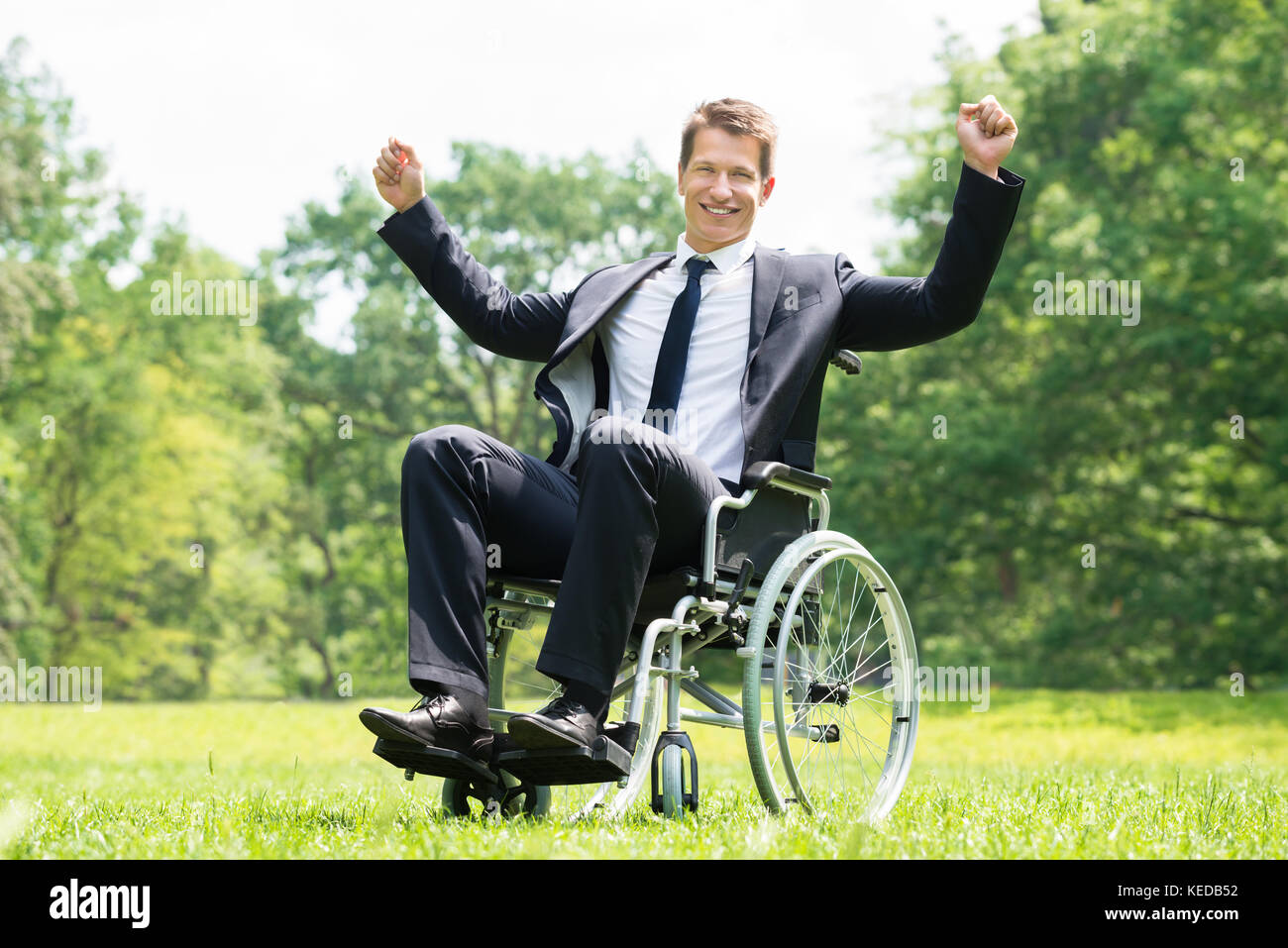 Felice giovane uomo disabili su sedia a rotelle con i bracci sollevati in posizione di parcheggio Foto Stock