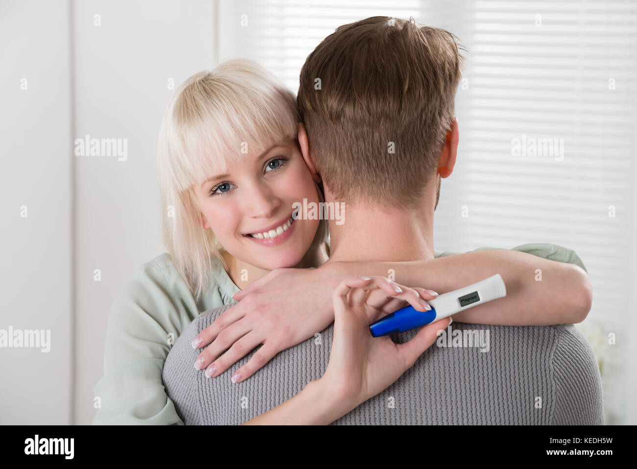 Felice giovane donna con test di gravidanza abbracciando l uomo a casa Foto Stock