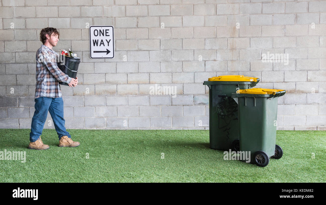 L'uomo portare rifiuti plastici di riciclo nel riciclare bidoni gialli per promuovere il concetto di ambiente di "ciclo' Foto Stock