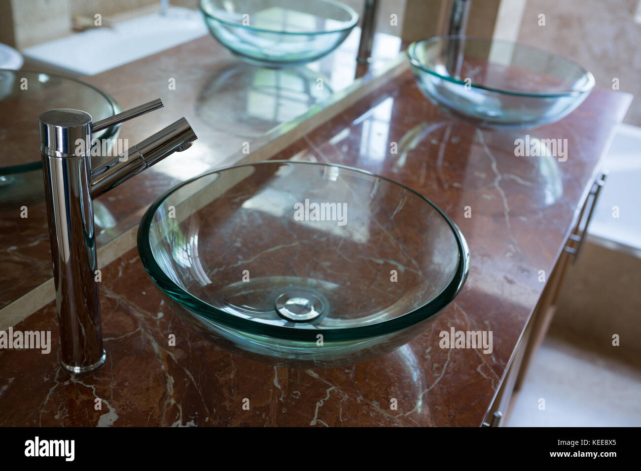 Lavandini di vetro con acciaio rubinetti installati sulla piattaforma di marmo nella stanza da bagno Foto Stock