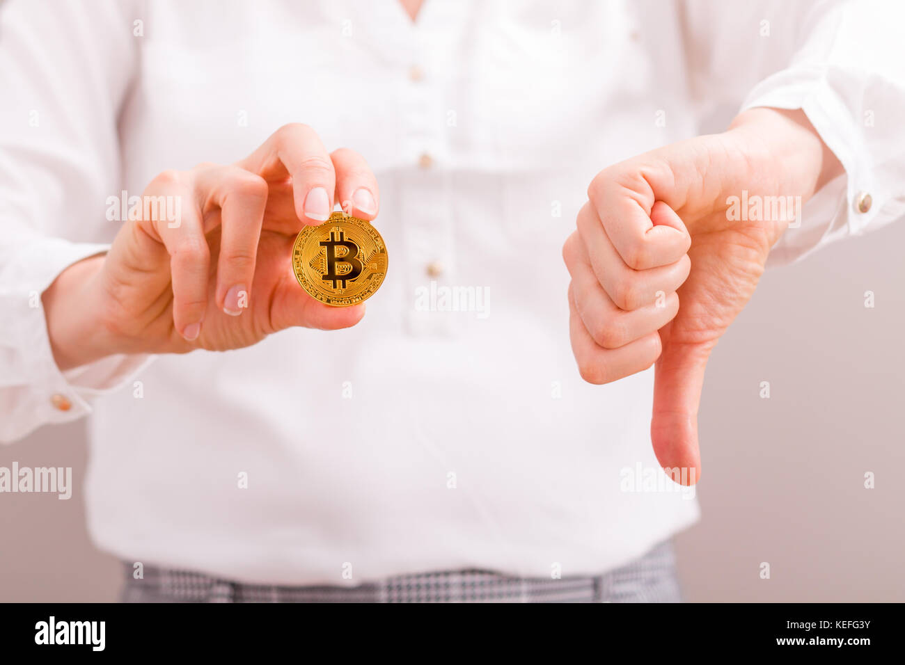 Imprenditrice tenendo premuto il bitcoin moneta in oro e il pollice verso il basso, preoccuparsi della perdita di valore. Foto Stock