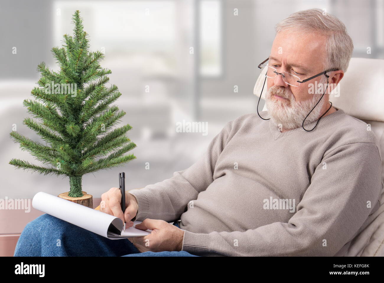 Il vecchio uomo che fa un elenco di acquisti su un foglio di carta con una penna accanto a un non decorato abete per vacanze di natale Foto Stock