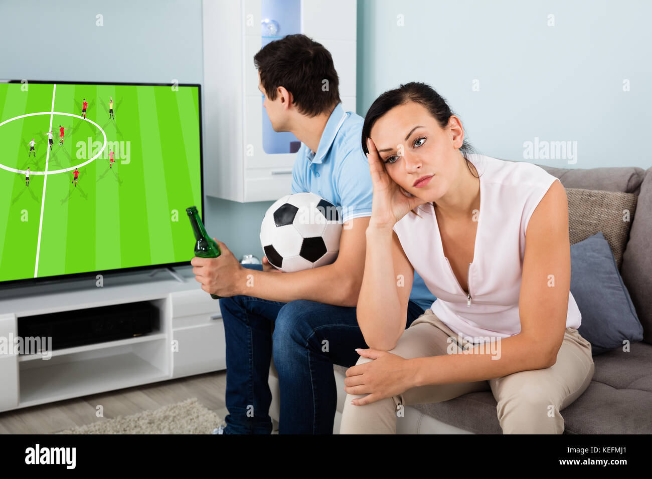 Triste donna seduta accanto a un uomo impegnato a guardare lo sport in TV a casa Foto Stock