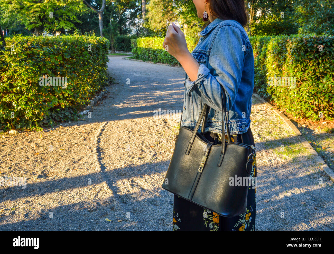 Una piscina esterna ritratto di una giovane donna, casualmente vestito, guardando avanti e tenendo una borsa nera Foto Stock