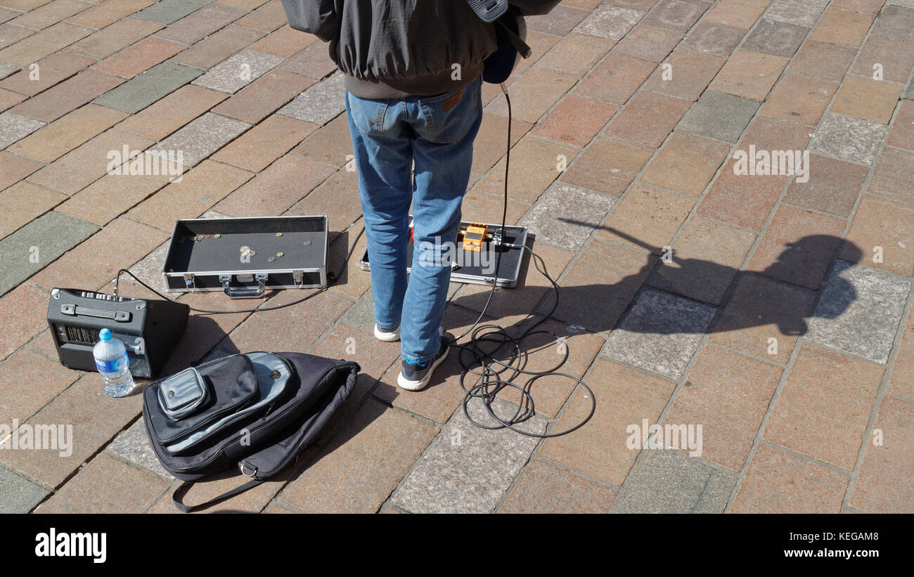 Glasgow suonatore ambulante di musica su strada il posizionamento sul marciapiede con guitar caso ombra in una giornata di sole visto da dietro Foto Stock