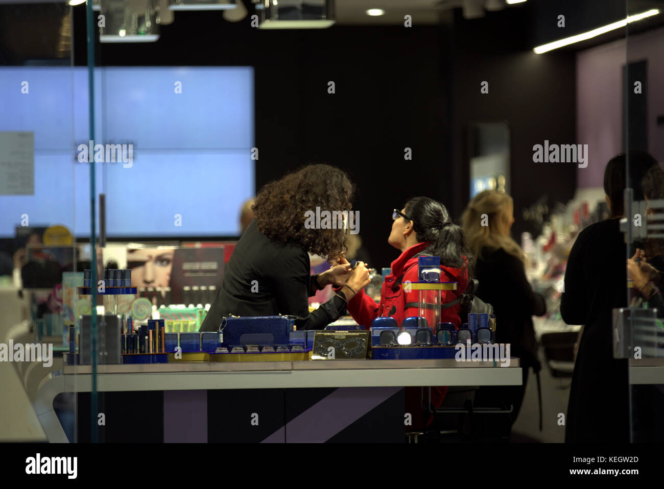 Preso dalla strada pubblica attraverso porte aperte estetista fa una dimostrazione di trucco su un cliente in un salone di bellezza shop visto da dietro Foto Stock