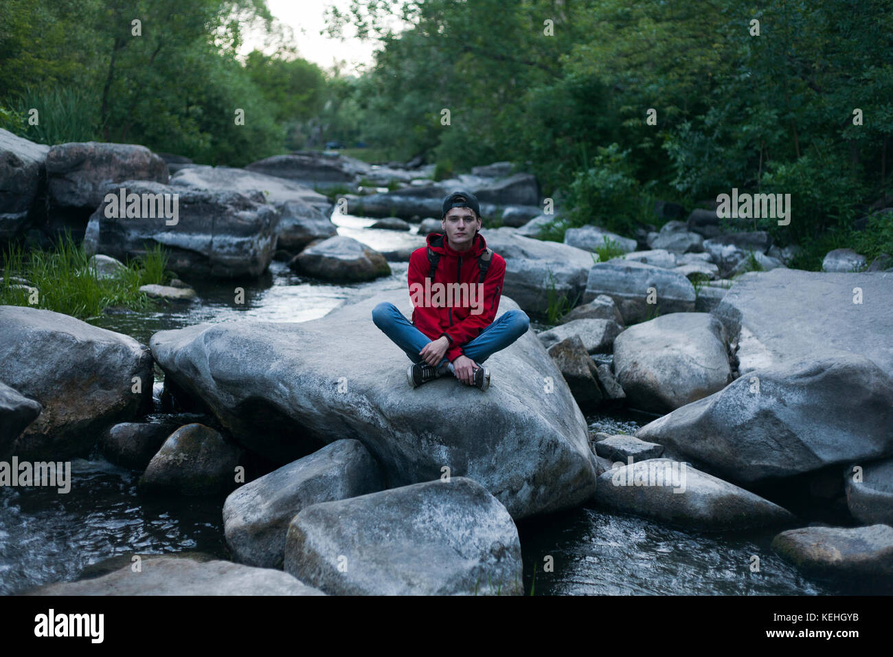 Uomo caucasico seduto sulla roccia nel fiume Foto Stock